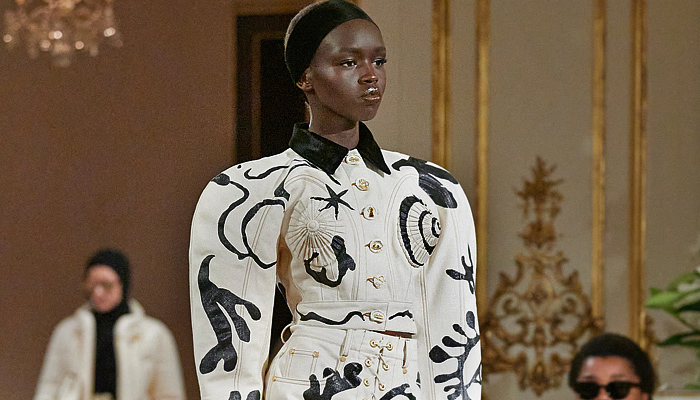 Schiaparelli 2023-2024 Fall Autumn Winter Womens Runway Collection - Paris Fashion Week Femme PFW - Hand-Painted Stencils Dove Keyhole Anatomy Silhouette Surrealist Bijoux Gold Buttons  Seashell Turtleneck Sweater Fur Velvet Blazer Head Wrap Headband Leg O'Mutton Sleeves Wool Quilted Puffer Parka Pillow Coat Cardigan Denim Jeans Worker Pants Pockets Pleats Miniskirt Cuffs Strapless Peplum Dress Cutout Coatdress Cone Breasts Tights Heels Face Bag Wrapped Heels Balaclava